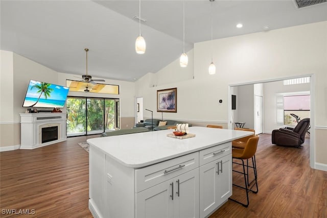 kitchen with dark hardwood / wood-style floors, high vaulted ceiling, white cabinets, a kitchen bar, and a center island