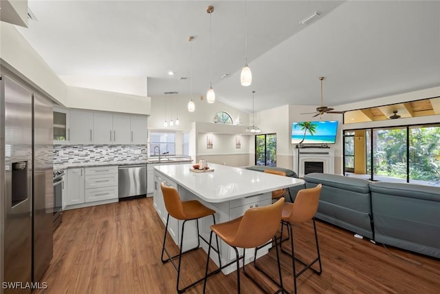 kitchen with stainless steel appliances, a center island, a kitchen bar, decorative light fixtures, and vaulted ceiling