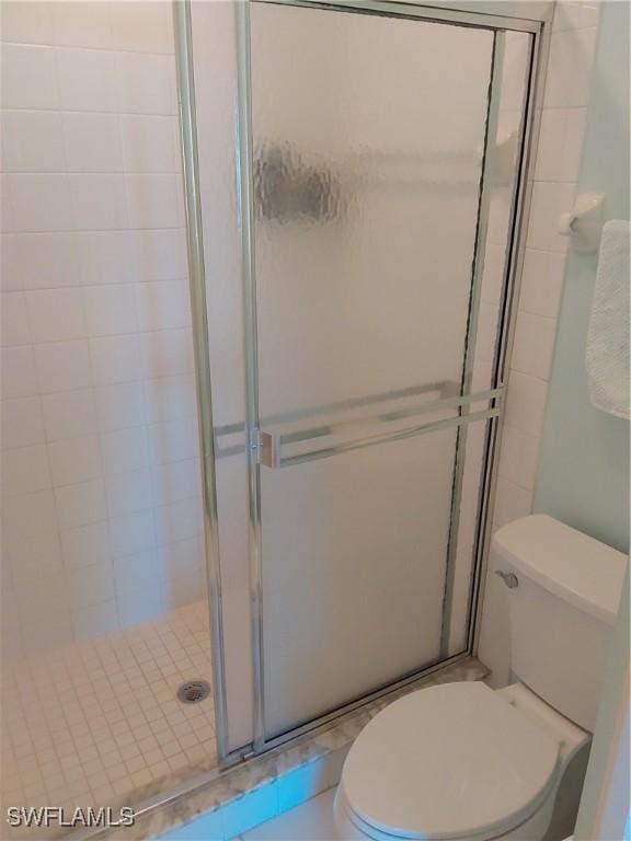 bathroom featuring a shower with door and toilet