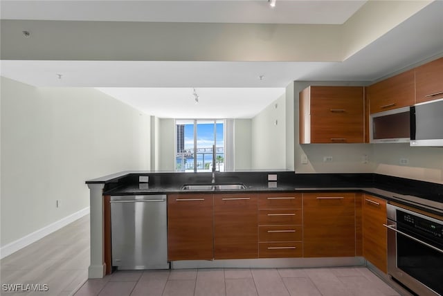 kitchen featuring rail lighting, sink, dark stone countertops, kitchen peninsula, and stainless steel appliances