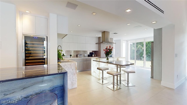 kitchen featuring island range hood, light stone countertops, white cabinets, decorative backsplash, and beverage cooler