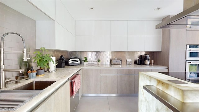 kitchen with wall chimney exhaust hood, sink, light tile patterned floors, stainless steel appliances, and decorative backsplash