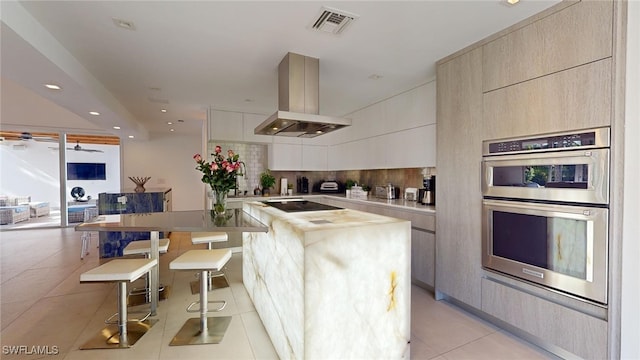 kitchen featuring double oven, tasteful backsplash, a kitchen breakfast bar, island exhaust hood, and a center island