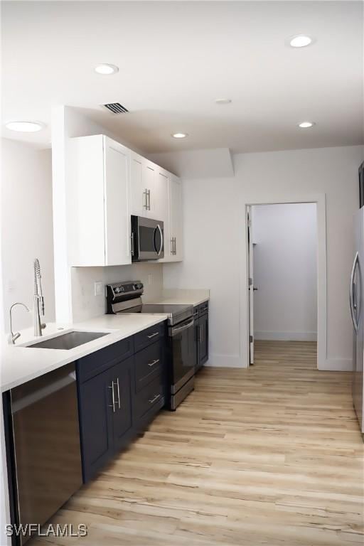 kitchen with stainless steel appliances, white cabinetry, sink, and light wood-type flooring