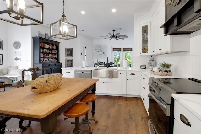 kitchen with dark wood-type flooring, appliances with stainless steel finishes, white cabinets, pendant lighting, and wall chimney range hood