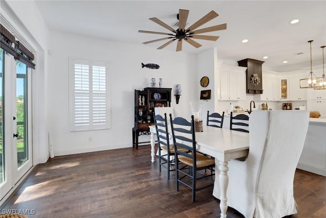 dining area with sink, ceiling fan with notable chandelier, and dark wood-type flooring