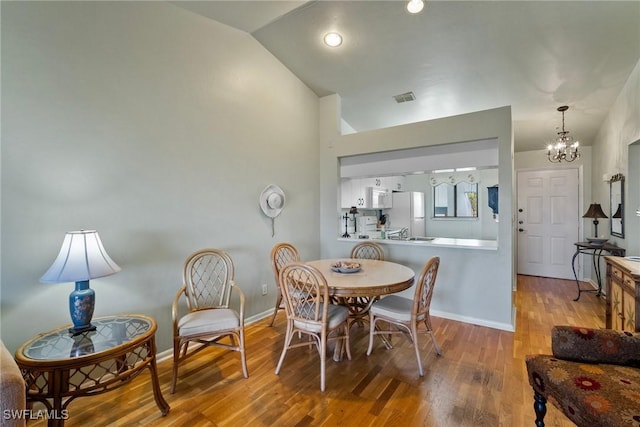 dining area featuring a chandelier, vaulted ceiling, and light hardwood / wood-style flooring