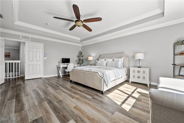 bedroom with a tray ceiling, wood finished floors, ornamental molding, and visible vents