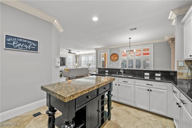 kitchen featuring pendant lighting, white cabinetry, sink, dark stone countertops, and ornamental molding