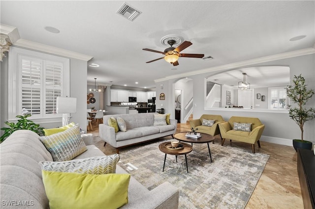 living area featuring baseboards, crown molding, visible vents, arched walkways, and ceiling fan with notable chandelier