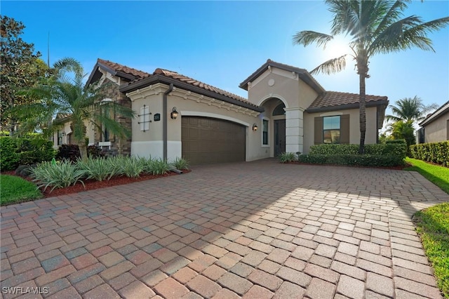 mediterranean / spanish-style house featuring an attached garage, a tile roof, decorative driveway, and stucco siding