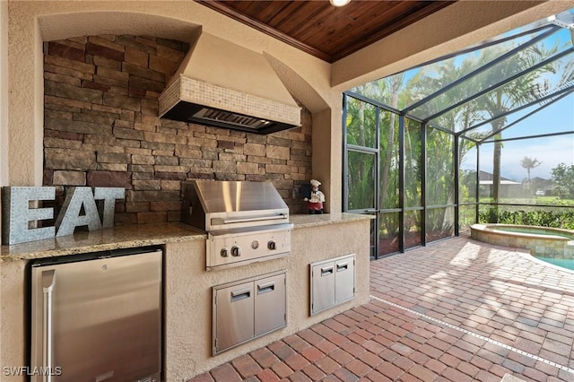 view of patio / terrace featuring glass enclosure, a grill, a pool with connected hot tub, and exterior kitchen