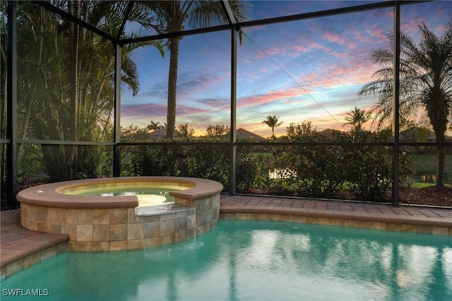 pool at dusk featuring a lanai and a pool with connected hot tub