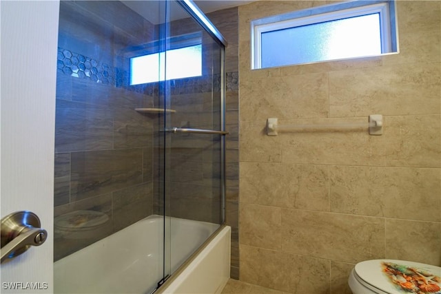 bathroom with a healthy amount of sunlight, bath / shower combo with glass door, and toilet