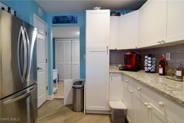 kitchen featuring light stone countertops, stainless steel refrigerator, and white cabinets