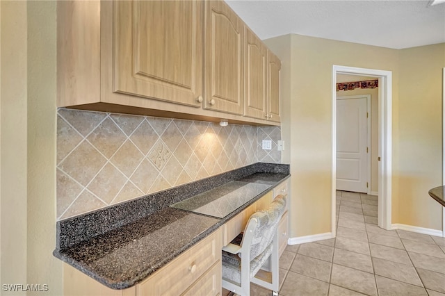 kitchen featuring light tile patterned flooring, built in desk, tasteful backsplash, dark stone countertops, and light brown cabinets