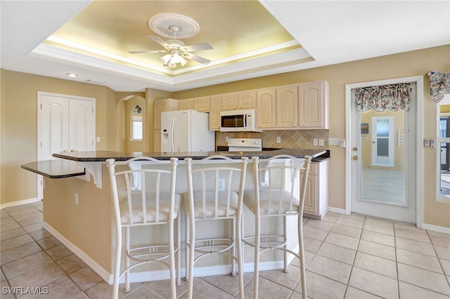 kitchen with white appliances, a tray ceiling, a center island, and a breakfast bar