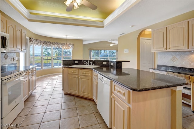 kitchen with white appliances, a raised ceiling, and an island with sink