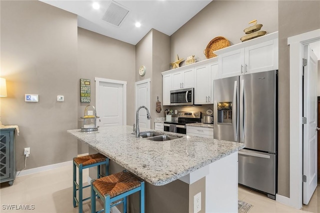 kitchen featuring a breakfast bar area, appliances with stainless steel finishes, a kitchen island with sink, white cabinetry, and light stone counters