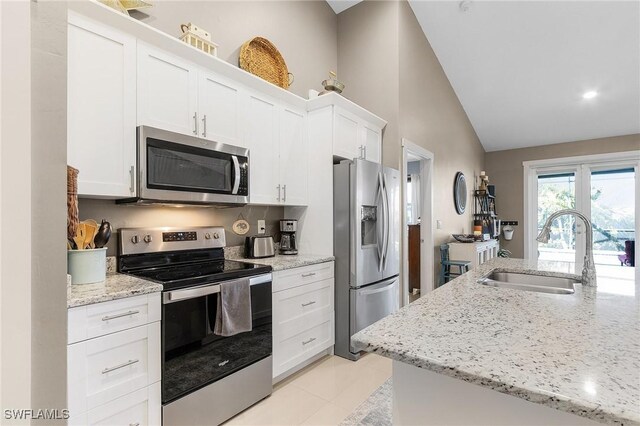 kitchen featuring vaulted ceiling, white cabinetry, sink, stainless steel appliances, and light stone countertops