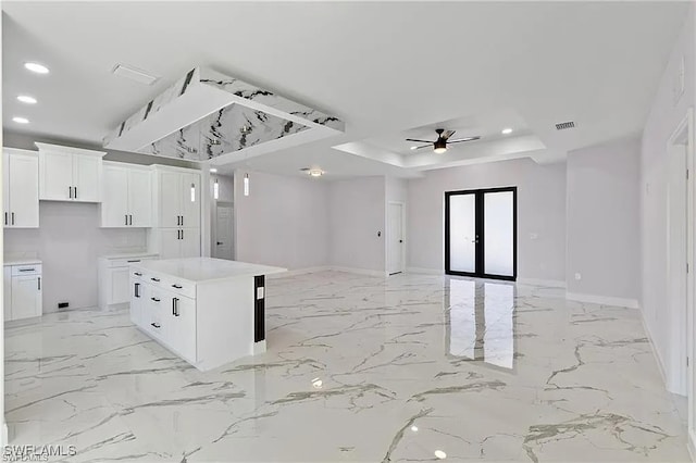 kitchen featuring french doors, white cabinetry, a raised ceiling, a kitchen island, and ceiling fan