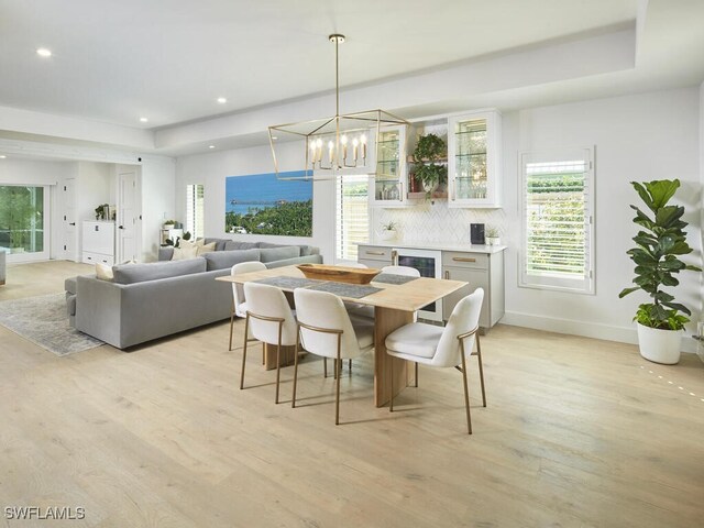 dining space with a raised ceiling, a notable chandelier, wine cooler, and light hardwood / wood-style floors