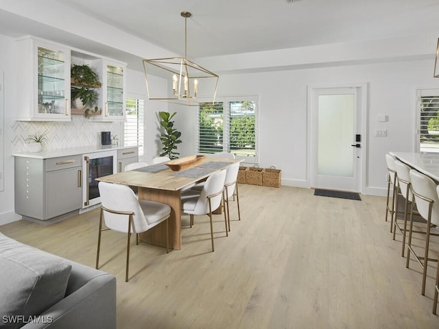 dining room featuring wine cooler, light wood-style flooring, baseboards, and an inviting chandelier