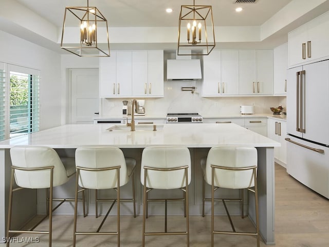 kitchen featuring light wood finished floors, high end white fridge, a sink, light countertops, and backsplash