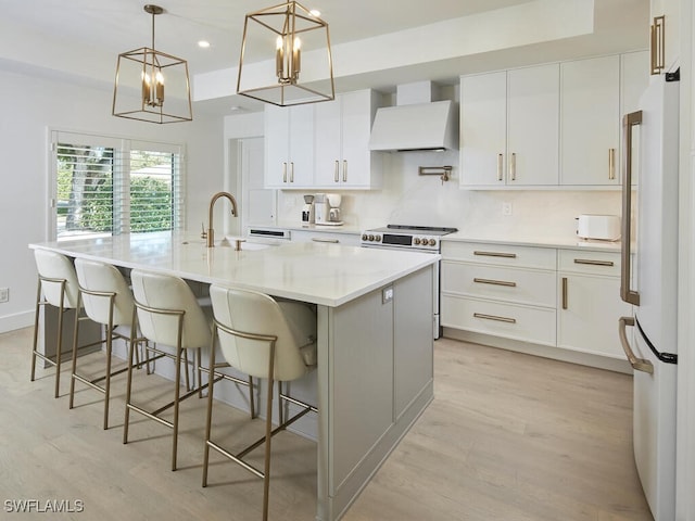 kitchen with stainless steel range, custom range hood, freestanding refrigerator, a sink, and light wood-type flooring