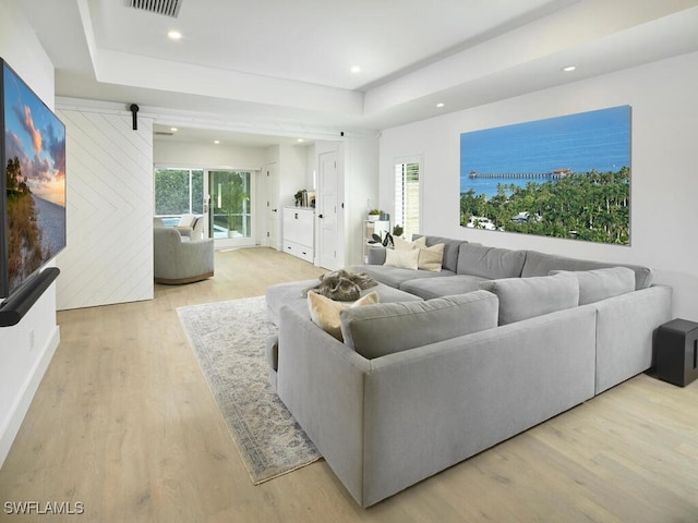 living room with light wood-style flooring, a raised ceiling, a wealth of natural light, and recessed lighting