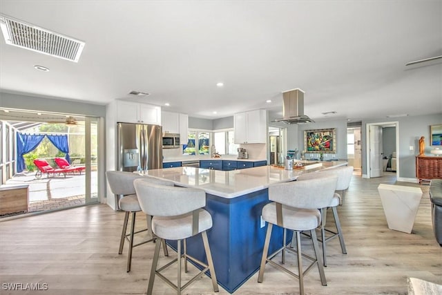 kitchen featuring a breakfast bar area, light hardwood / wood-style flooring, island exhaust hood, stainless steel appliances, and white cabinets