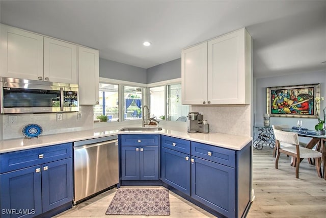 kitchen with sink, stainless steel appliances, white cabinets, blue cabinets, and decorative backsplash