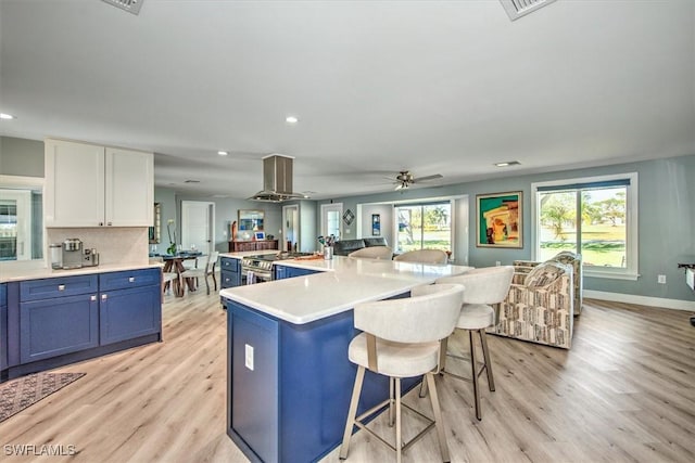 kitchen with blue cabinets, light hardwood / wood-style flooring, an island with sink, island exhaust hood, and white cabinets