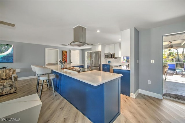 kitchen featuring appliances with stainless steel finishes, white cabinetry, a kitchen bar, island exhaust hood, and light hardwood / wood-style flooring