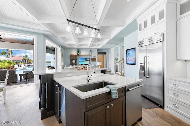 kitchen with coffered ceiling, sink, white cabinetry, a center island with sink, and appliances with stainless steel finishes