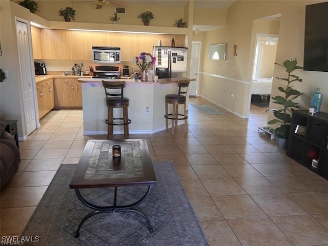 kitchen with light tile patterned floors, a breakfast bar area, ceiling fan, stainless steel appliances, and a center island