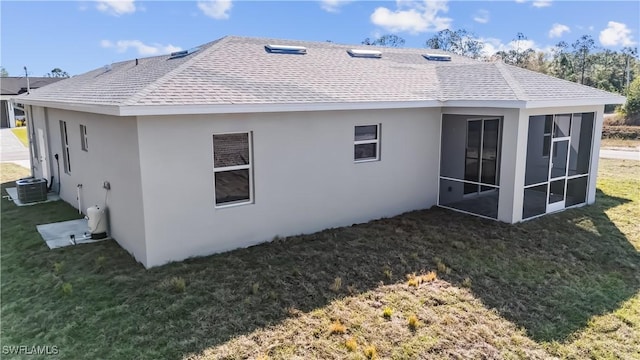 rear view of property with central AC, a sunroom, and a lawn