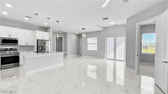 kitchen with appliances with stainless steel finishes, a wealth of natural light, white cabinetry, sink, and a kitchen island with sink