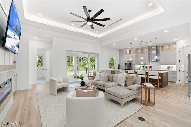 living room featuring ceiling fan, a raised ceiling, a high ceiling, and light wood-type flooring