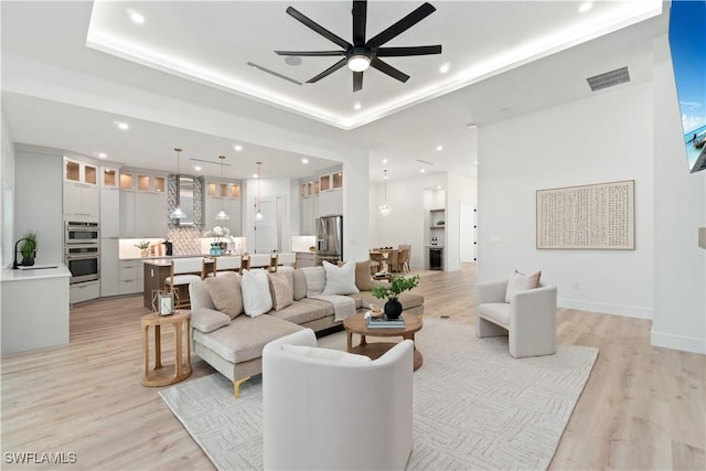 living room featuring ceiling fan, a raised ceiling, sink, and light wood-type flooring