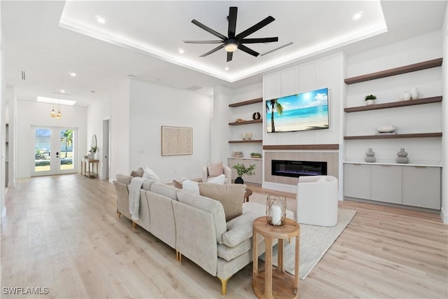 living room with a tray ceiling, a fireplace, french doors, and light wood-type flooring