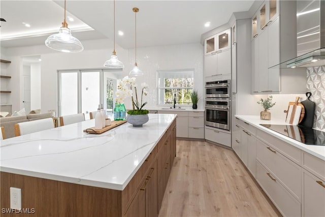 kitchen featuring sink, white cabinetry, wall chimney exhaust hood, decorative light fixtures, and stainless steel double oven