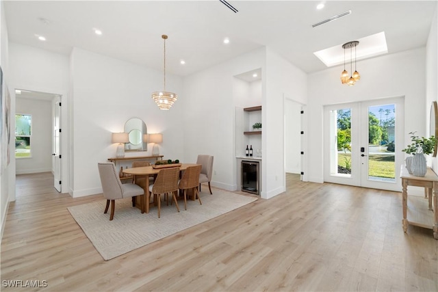 dining area featuring french doors, a towering ceiling, light wood-type flooring, and a notable chandelier