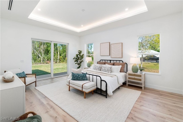 bedroom with a raised ceiling, light hardwood / wood-style flooring, and access to outside