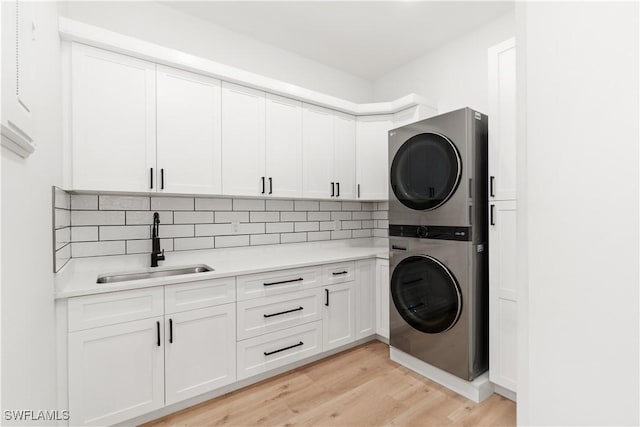 laundry room featuring stacked washer and dryer, sink, light hardwood / wood-style flooring, and cabinets