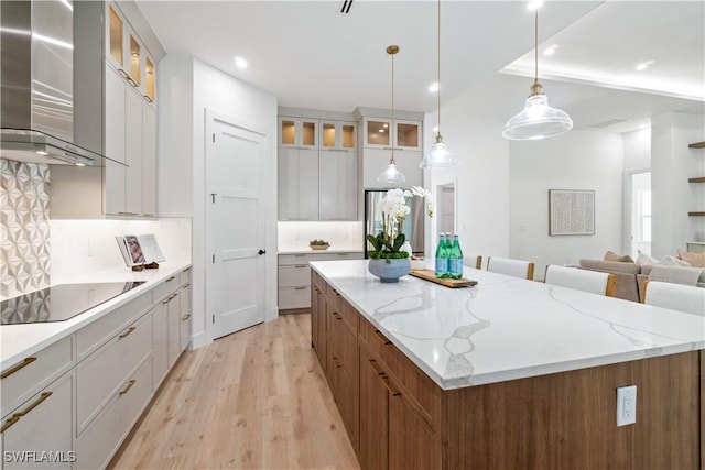 kitchen with white cabinetry, hanging light fixtures, a large island, black electric stovetop, and wall chimney exhaust hood