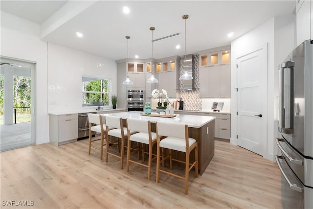 kitchen with decorative light fixtures, a center island, stainless steel appliances, wall chimney range hood, and light wood-type flooring