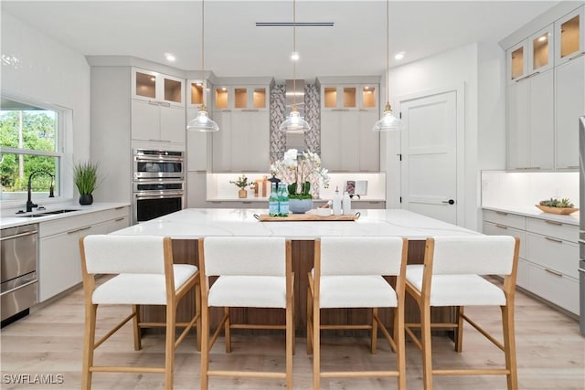 kitchen with a spacious island, decorative light fixtures, light stone countertops, and sink