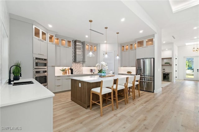 kitchen with sink, pendant lighting, stainless steel appliances, a large island, and wall chimney range hood