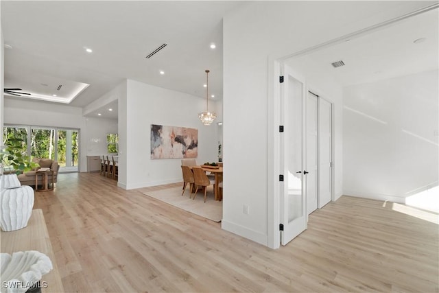 corridor with light hardwood / wood-style flooring and a notable chandelier